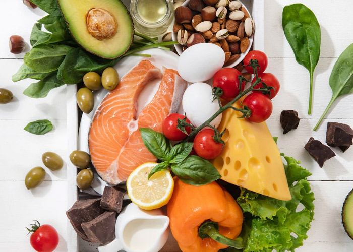 Alguns alimentos em uma bandeja. Podemos ver uma fatia de salmão, abacate, azeite de oliva e algumas castanhas