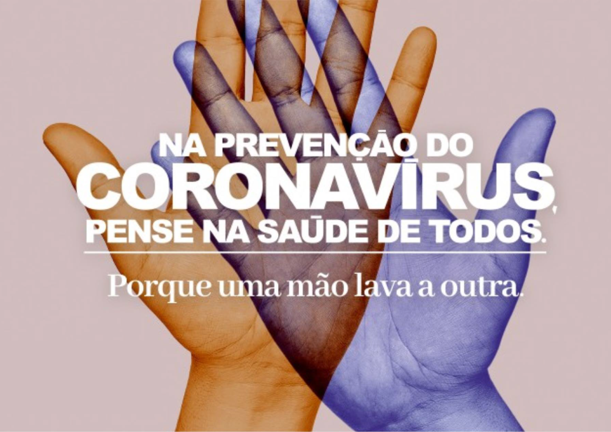 Uma mão, na vertical, de cor azul, está cruzada em cima de uma mão de pele branca. Em cima das duas mãos, está escrito em letras pequenas brancas “na prevenção do”. No centro, em letras brancas maiores, está escrito “coronavírus”, logo abaixo, em letras brancas e menores, está escrito “pense na saúde de todos”. Na parte inferior, há a frase “porque uma mão lava a outra”.
