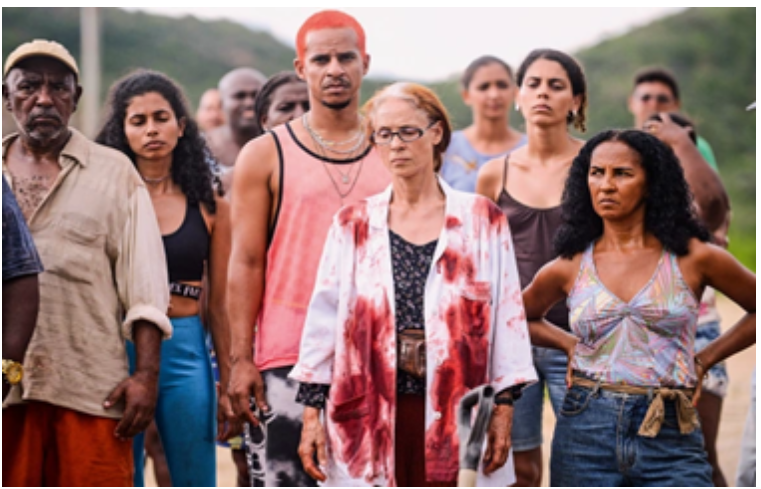 Recorte de cena diurna, ao ar livre, do filme Bacurau, com um grupo de atores posicionados de frente. 