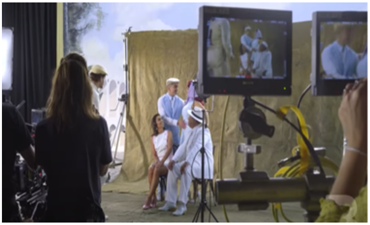 Fotografia da gravação do clipe da cantora Anitta. Atores sentados ao fundo das câmeras. 