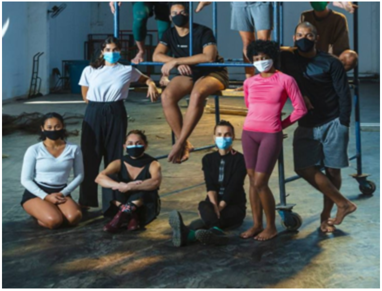 Fotografia dos dançarinos da companhia de dança, sentados no local de ensaio. 
